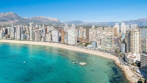 Un paisaje costero con edificios altos, una playa y montañas al fondo.