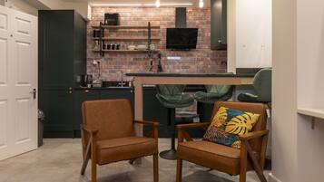 A compact kitchen with a brick backsplash, a flat-screen TV, and a dining area with two chairs and a table.