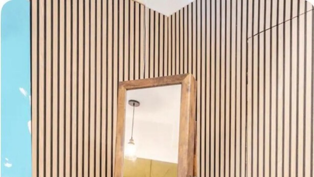 Uno specchio con cornice in legno in una stanza con rivestimento in legno verticale.