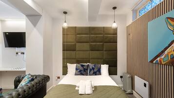 A modern hotel room with a green quilted bed, a leather sofa, a flat-screen TV, and a painting on the wall.