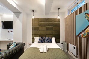 Une chambre d’hôtel moderne avec un lit matelassé vert, un canapé en cuir, un téléviseur à écran plat et un tableau au mur.
