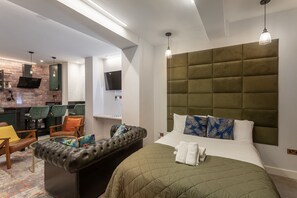 Una habitación de hotel moderna con una cama grande, un sofá de cuero, un pequeño comedor y un televisor montado en la pared.