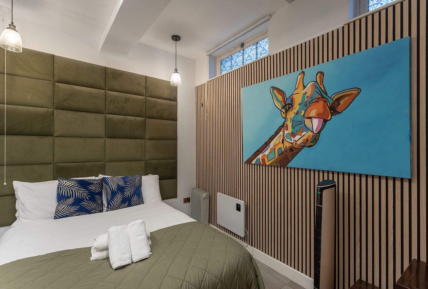 A modern bedroom with a tufted headboard, a large painting of a giraffe, and a radiator.