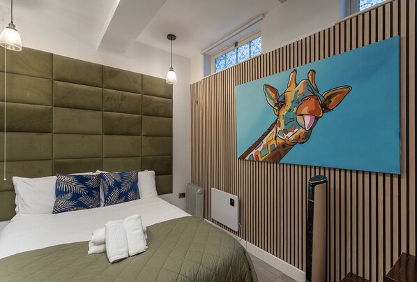 A modern bedroom with a tufted headboard, a large painting of a giraffe, and a radiator. - Aldgate London City Basement Urban Hideaway 1 (London)