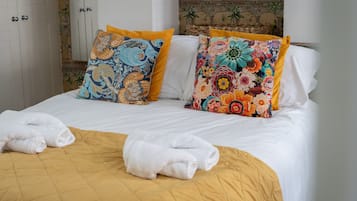 A bed with a yellow bedspread, two pillows with floral patterns, and two folded white towels.