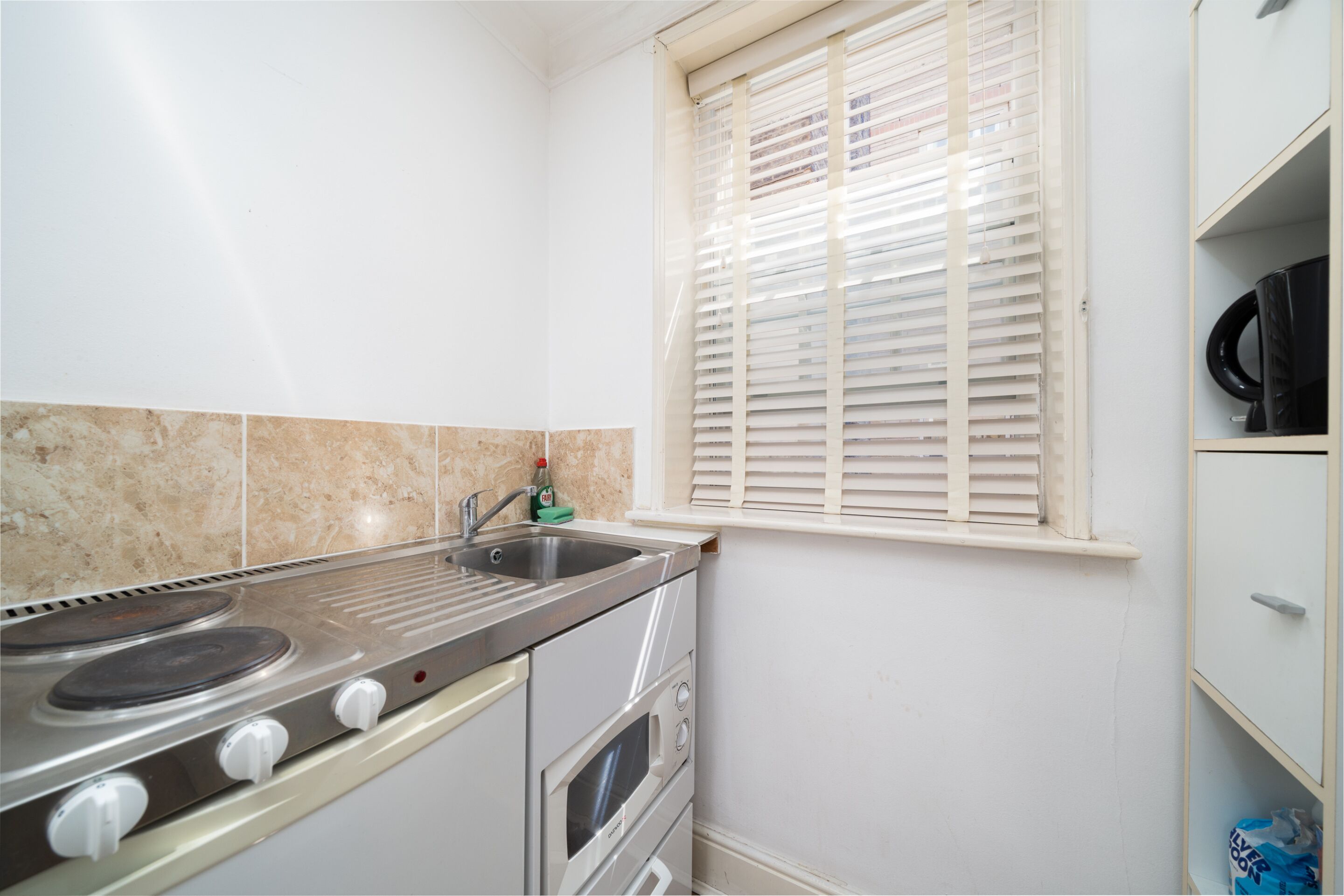 Eine Küche mit Herd, Backofen, Spüle und einem Fenster mit Jalousien.