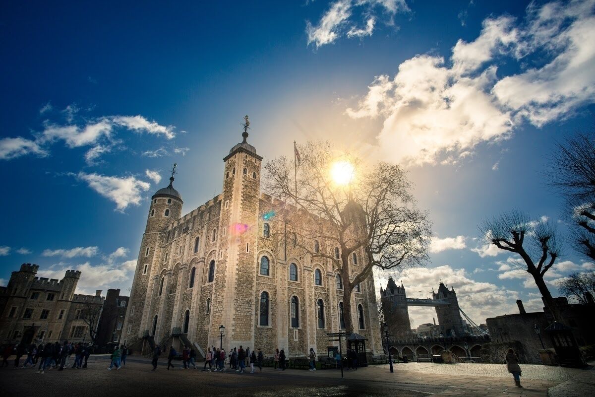A historic building with a prominent tower and arched windows, situated in a public square with a clear sky and sunlight.