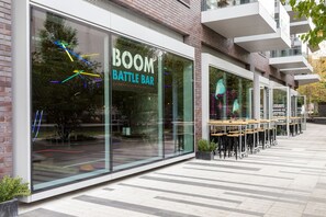 Een modern gebouw met een glazen gevel en de naam 'BOOM BATTLE BAR' op het raam.
