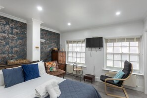 Een slaapkamer met een bed, een stoel, een bureau, een televisie en een raam.