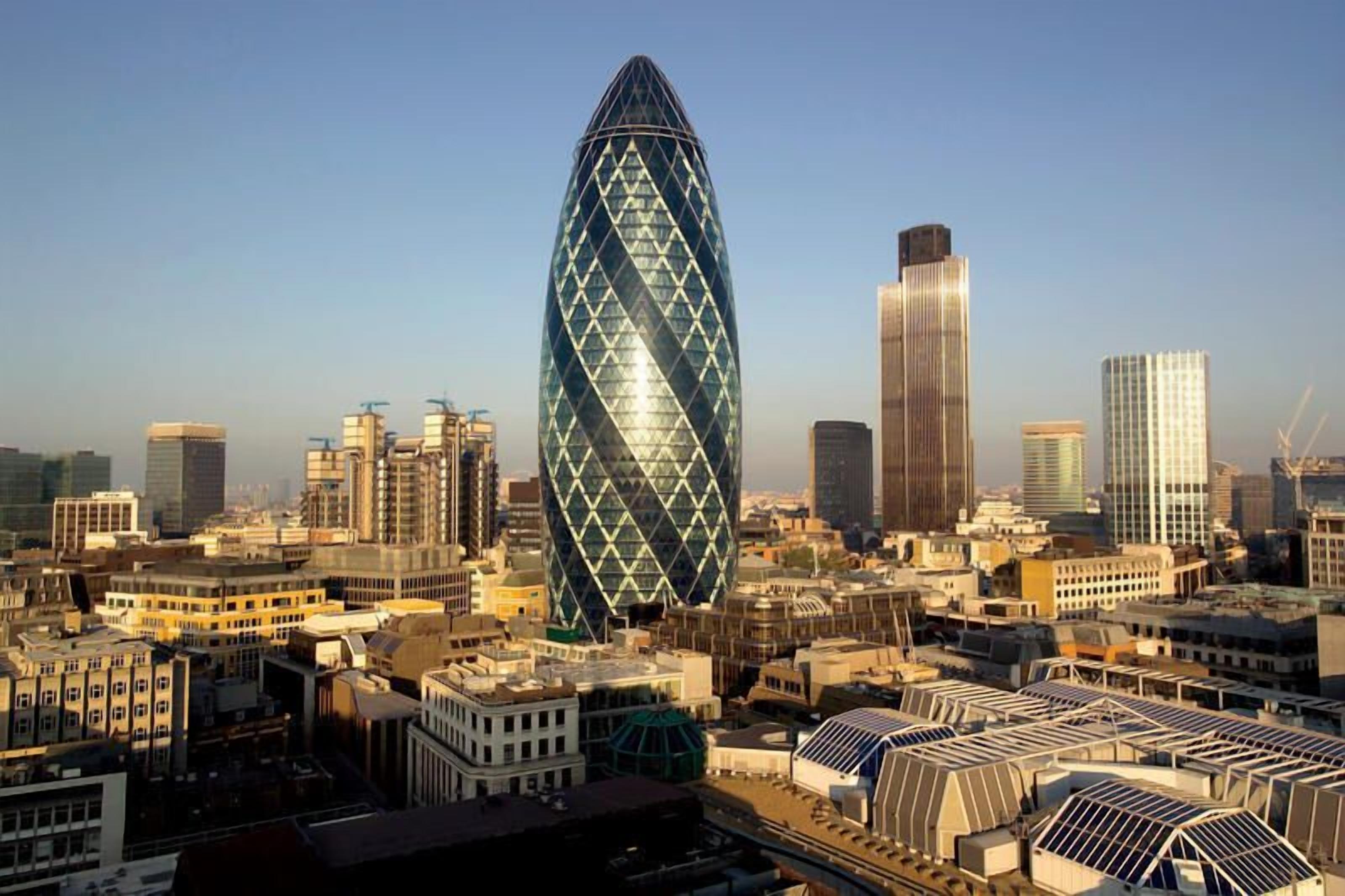 A cityscape with a prominent building featuring a diamond pattern, surrounded by various other buildings and construction sites.