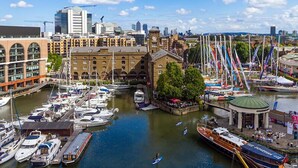 A marina with various boats docked, a clock tower, and a mix of modern and traditional buildings. - Aldgate London City Boutique Cosy Studio 4 (London)