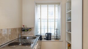 A kitchen with a stove, sink, and window with blinds. - Aldgate London City Charming Studio 5 (London)
