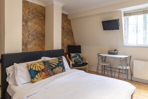 Ein Hotelzimmer mit einem Bett, einem Sessel, einem kleinen Tisch und einem an der Wand befestigten Fernseher.