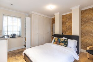 A bedroom with a bed, a wardrobe, a window with blinds, and a wall with a patterned design.