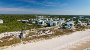 Vue aérienne d’un quartier résidentiel situé sur la côte, avec des immeubles modernes à plusieurs étages, une plage de sable et un ciel dégagé.