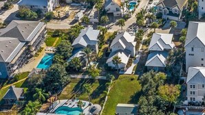 Vue aérienne d’un quartier résidentiel situé sur la côte, avec des maisons, une plage et une piscine.