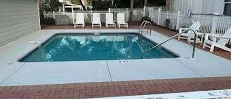 A rectangular swimming pool with a white deck, surrounded by a white fence and trees.