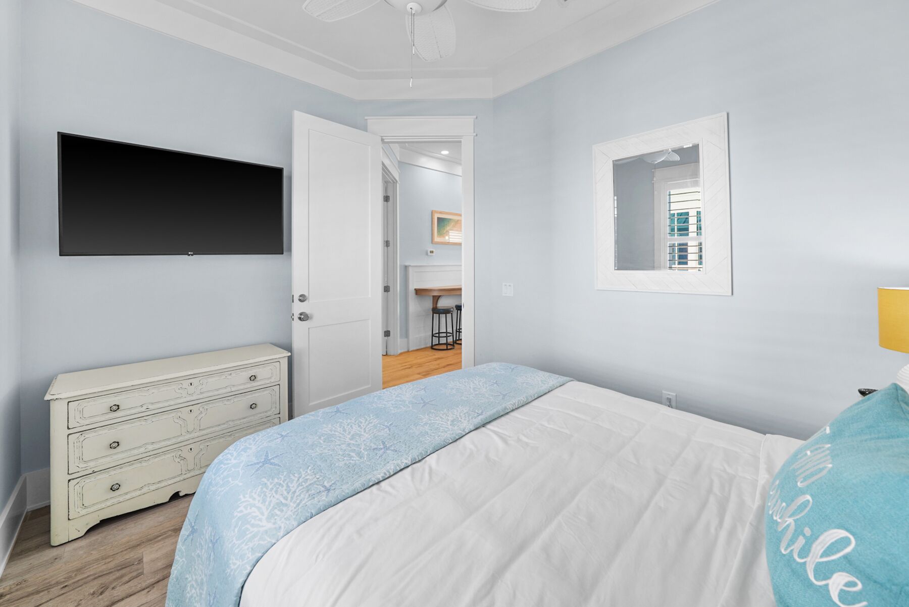 Une chambre à coucher comprenant un lit, une commode, un téléviseur et une porte donnant sur un coin cuisine.
