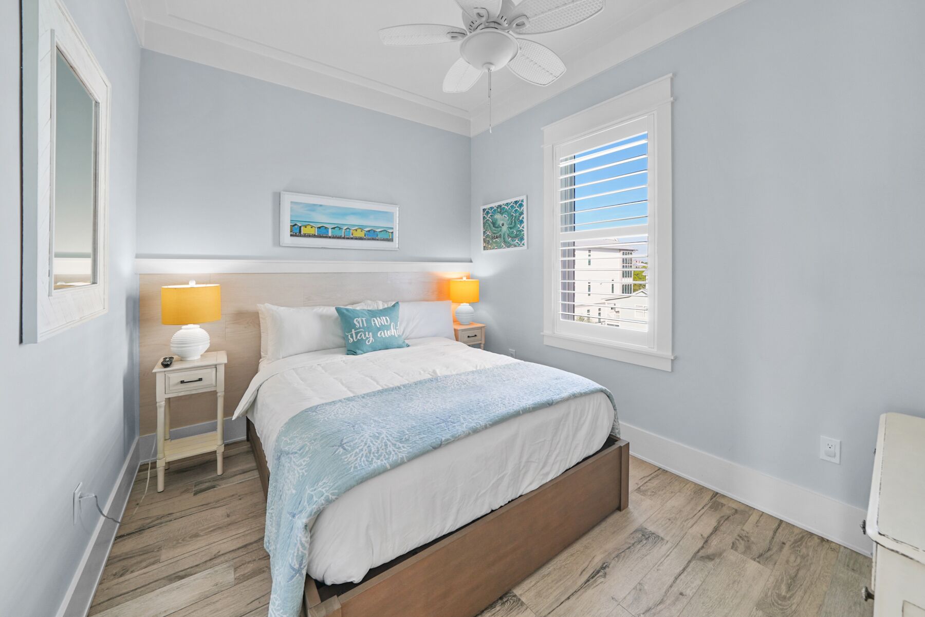 Une chambre à coucher comprenant un lit, deux tables de chevet avec des lampes, un ventilateur de plafond et une fenêtre avec des stores.