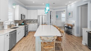 Une cuisine moderne avec des meubles blancs, un îlot central, des chaises en bois et une suspension bleue.