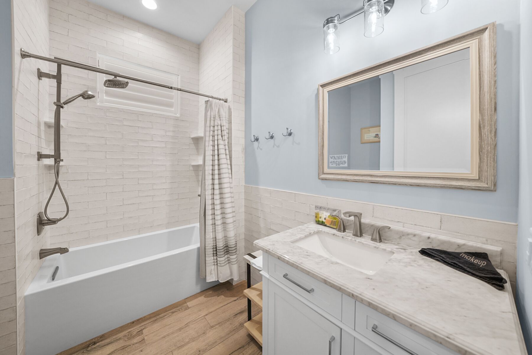 Une salle de bain avec une baignoire blanche, une douche dotée d’une pomme de douche protégée par une paroi de verre, un lavabo en marbre et un grand miroir.