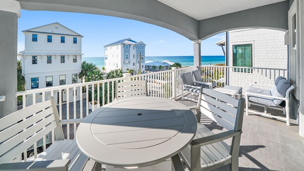 Un balcon avec une table ronde et des chaises, donnant sur une plage et des immeubles.