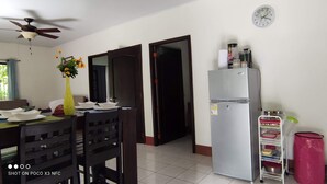 Una cucina funzionale con frigorifero, un tavolo da pranzo con sedie, una sveglia al muro e una ventola a soffitto.