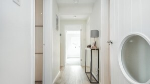 Un pasillo con suelo de madera, paredes blancas y una puerta con un ventanal circular.