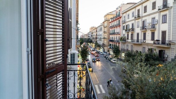 A balcony overlooking a street with buildings, a pedestrian, and vehicles.