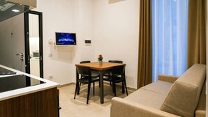 A compact living space with a kitchenette, a dining area with a table and chairs, a sofa, and a TV mounted on the wall.