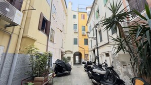 Um beco estreito com scooters estacionadas e uma motocicleta coberta, ladeado por edifícios com varandas e aparelhos de ar condicionado.