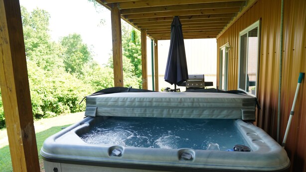 A hot tub with a wooden deck, a covered patio, and a view of greenery. - Honey Hole

 (Stockport)