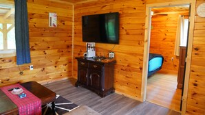 A wooden cabin interior with a TV, a small cabinet, a table with a red checkered tablecloth, and a bed with a blue pillow. - Honey Hole

 (Stockport)