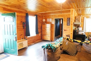 A wooden cabin interior with a door, a bench, a dresser, a sofa, and a window.