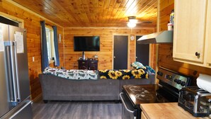 A cozy cabin interior with a kitchenette, a sofa, a flat-screen TV, and wooden walls. - Honey Hole

 (Stockport)