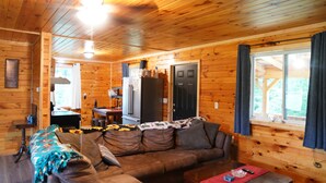A wooden cabin interior with a sofa, coffee table, and a kitchen area with a refrigerator. - Honey Hole

 (Stockport)