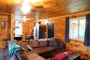 A wooden cabin interior with a sofa, coffee table, and a kitchen area with a refrigerator.