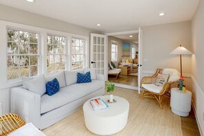 A spacious living room with a white sofa, a round coffee table, and a wicker chair. - Modern Cape Home in Hyannis walking distance to the beach & town! (Barnstable)