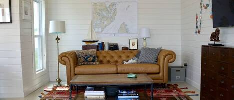Un salon chaleureux avec un canapé en cuir marron, une table basse sur laquelle sont posés des livres, un tapis à motifs et une carte accrochée au mur.