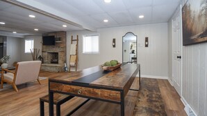 Un salon spacieux avec une longue table en bois, une cheminée en pierre et un grand miroir au mur.