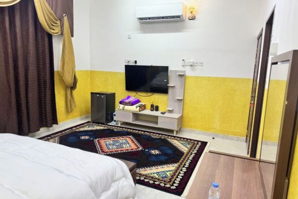 A hotel room with a bed, a TV, a small cabinet, and a colorful rug.