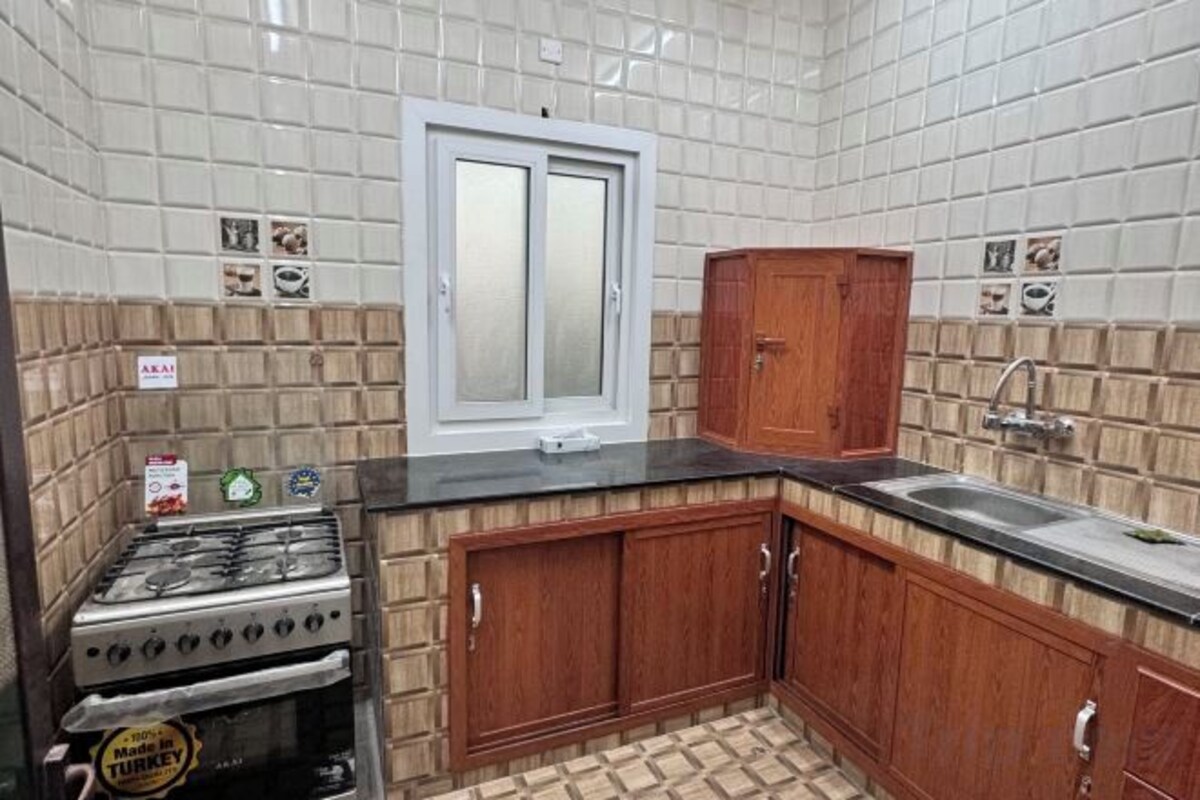 A kitchen with a gas stove, wooden cabinets, a window, and tiled walls.