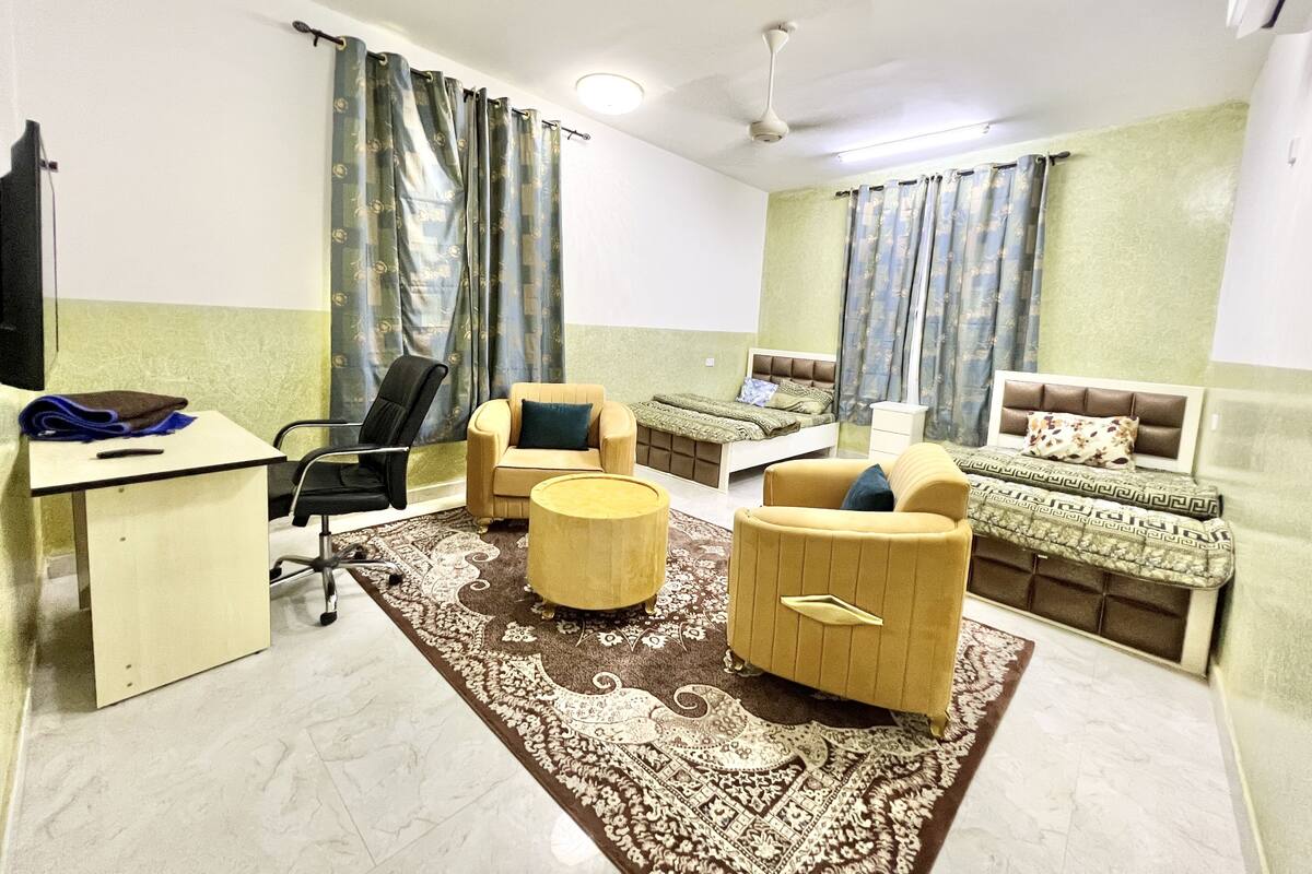 Habitación de hotel con cama, dos sillones, escritorio, silla, una mesita redonda y ventilador de techo.