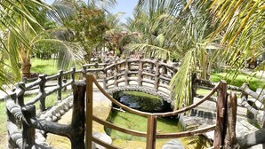 A stone pathway leading to a wooden bridge over a pond, surrounded by palm trees and greenery. - Cloud Cloud Farm Resort (Izki)