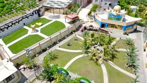 An aerial view of a resort with a pool, palm trees, and a building with a blue and white facade. - Cloud Cloud Farm Resort (Izki)