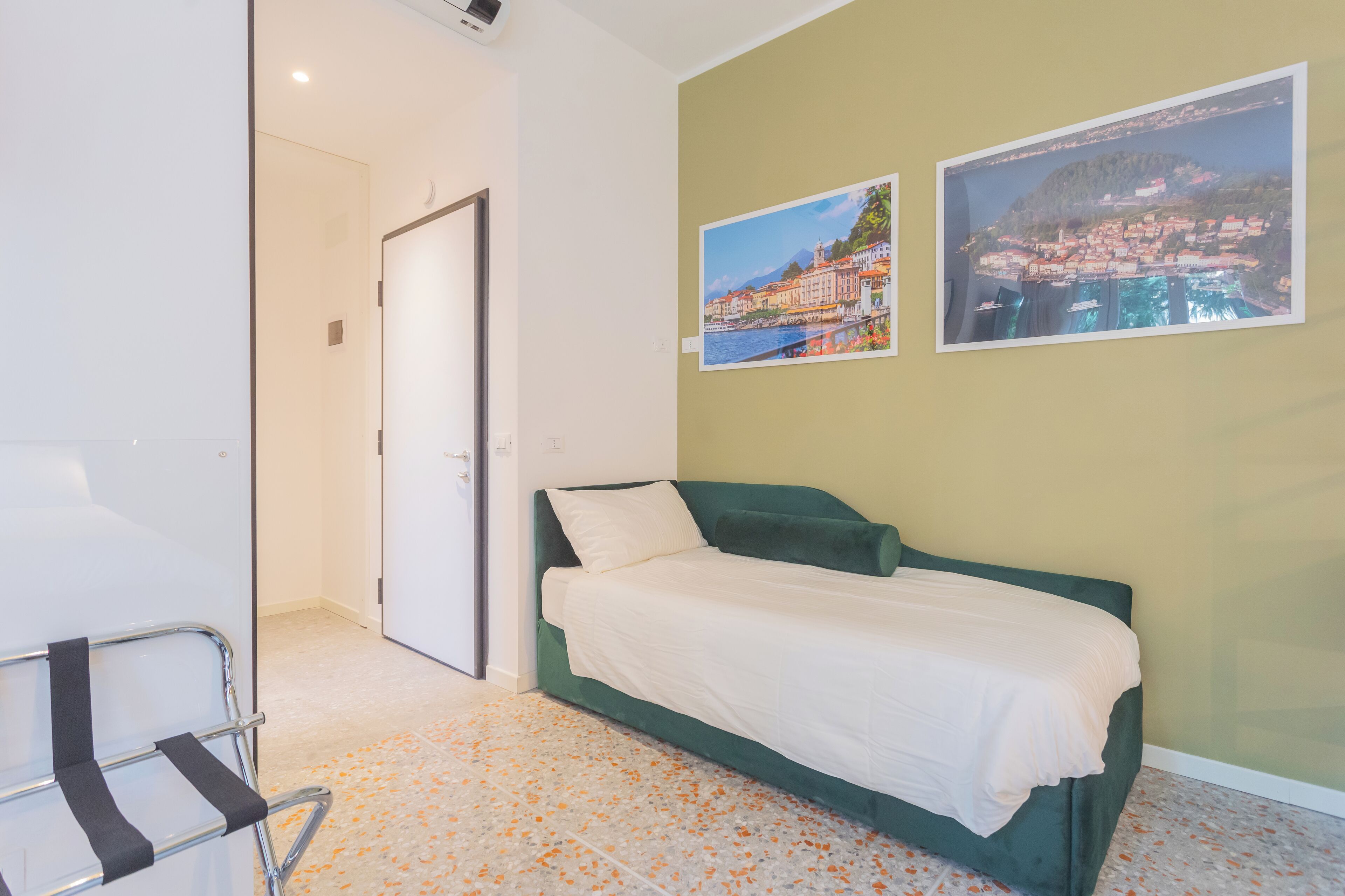 Een kamer met een groen bed, witte muren en twee ingelijste foto's.