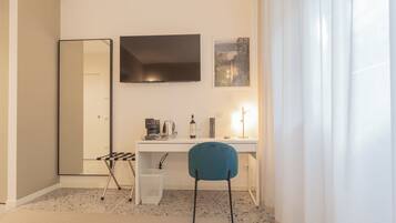 Une chambre d’hôtel moderne avec un bureau blanc, une chaise bleue, un grand miroir et un tableau encadré accroché au mur.