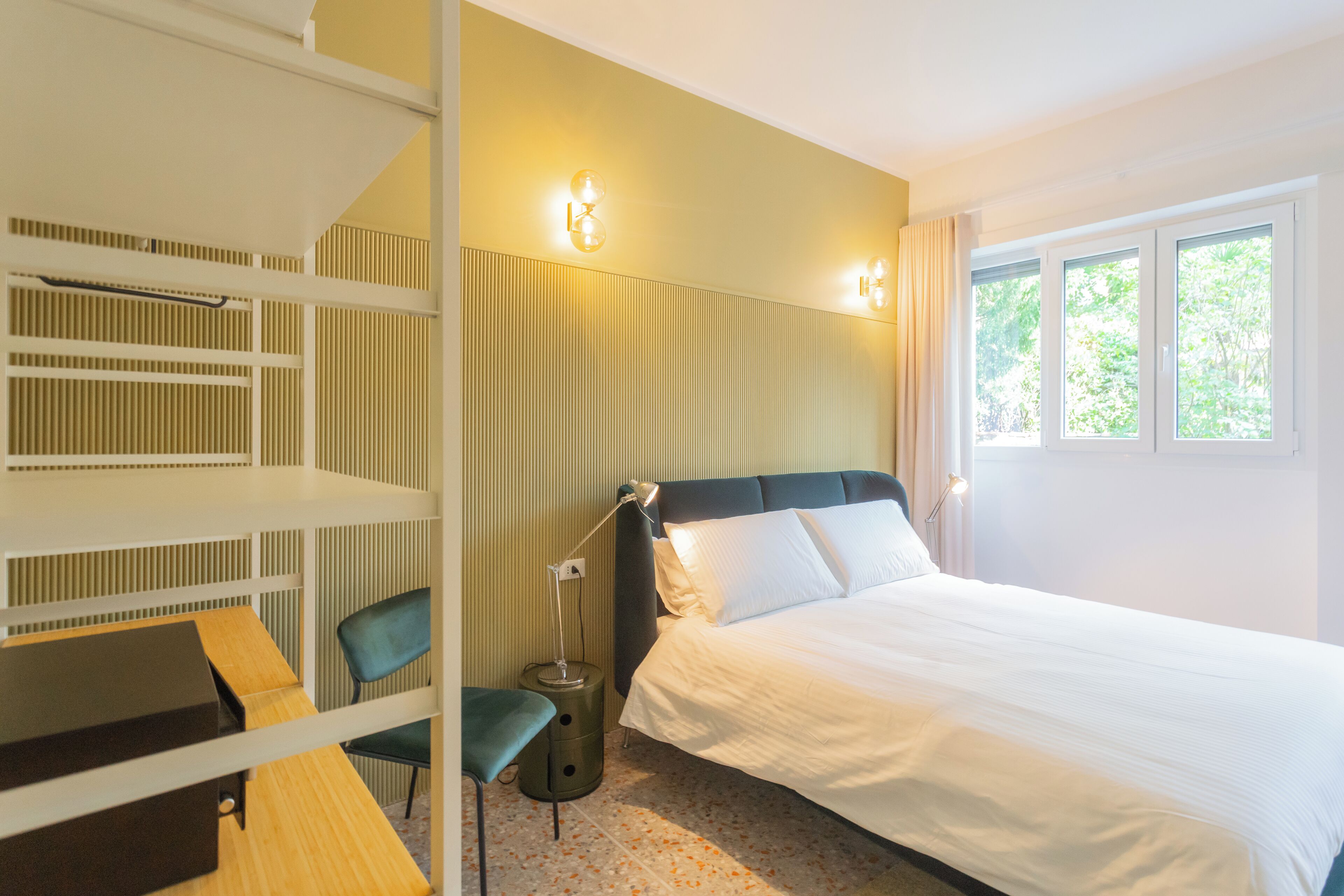 A hotel room with a bed, a desk, a chair, and a lamp.