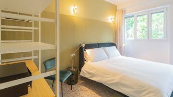A hotel room with a bed, a desk, a chair, and a lamp.