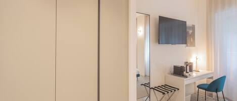 A modern hotel room with a white desk, a blue chair, a flat-screen TV, and a large mirror.